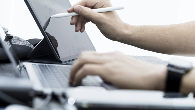 Foto mostrando manos en una computadora con un lapiz digital interactuando con una tableta